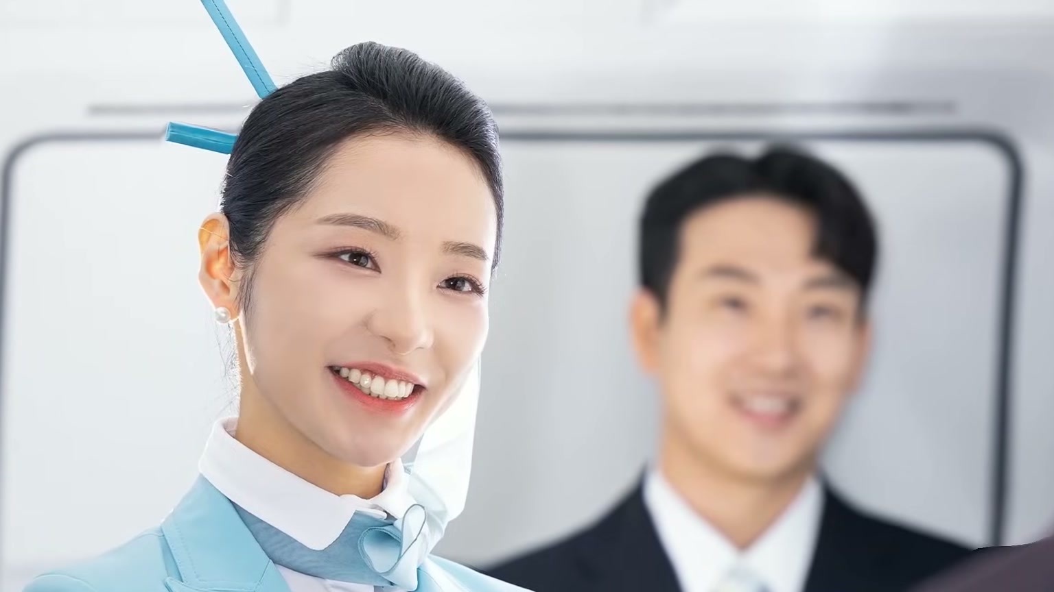 ลูกเรือ Korean Air ในยูนิฟอร์มสีฟ้าเซลาดอน ยิ้มอยู่ในห้องโดยสาร